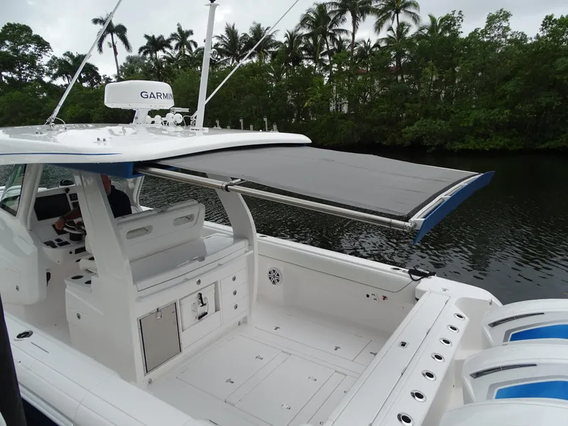 Slide: The Image of 2022 Intrepid 407 Panacea boat with canopy, docked near lush greenery. - 15