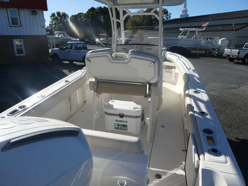 Slide: The Image of 2025 Boston Whaler 230 Outrage boat interior with seating and cooler, parked outdoors. - 3