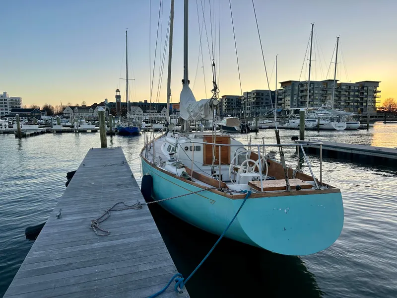 Slide: The Image of 1970 Hinckley 38 sailboat docked at marina during sunset, with cityscape in background. - 6