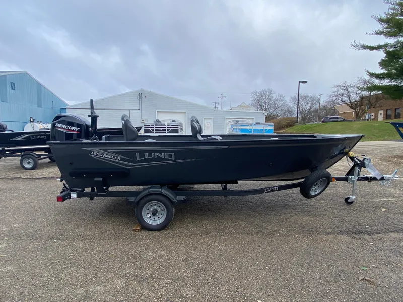 Slide: The Image of 2025 Lund 1650 Angler Tiller boat on trailer, parked outdoors. - 4