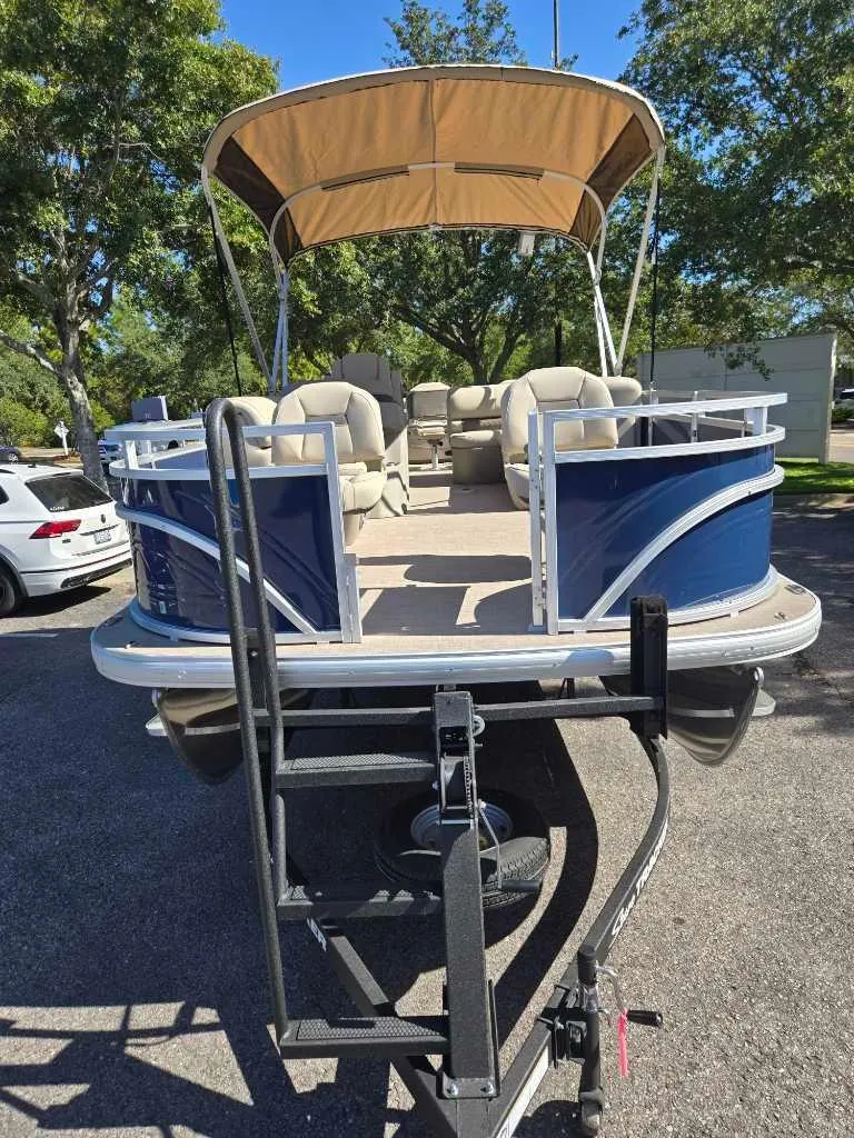 Slide: The Image of 2025 Sun Tracker Fishin' Barge 22 DLX pontoon boat on trailer, parked outdoors. - 2