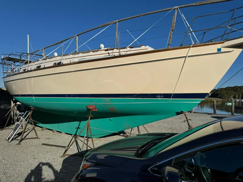 Slide: The Image of 1998 Island Packet 40 sailboat on stands, parked on gravel, under clear blue sky. - 1