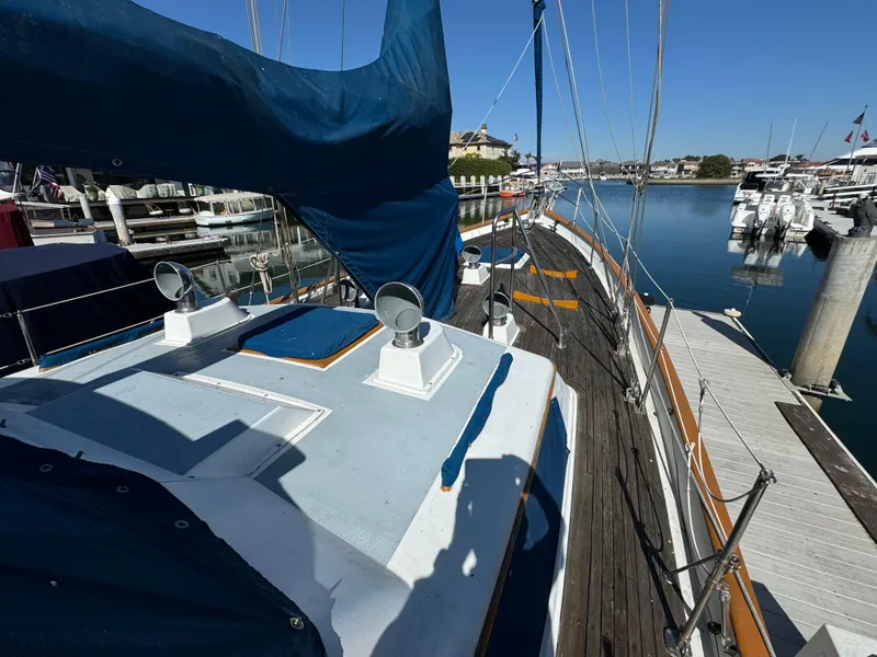 Slide: The Image of 1984 Transpacific Marine Ketch docked at marina, featuring blue sails and wooden deck. - 10