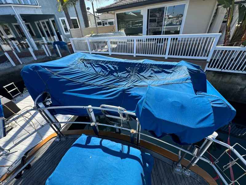 Slide: The Image of 1984 Transpacific Marine Ketch with blue covers docked near waterfront homes. - 24