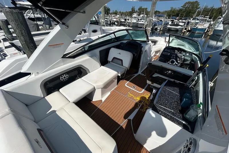 Slide: The Image of 2015 Monterey 288 Super Sport boat interior with white seating and wood flooring at a marina. - 2