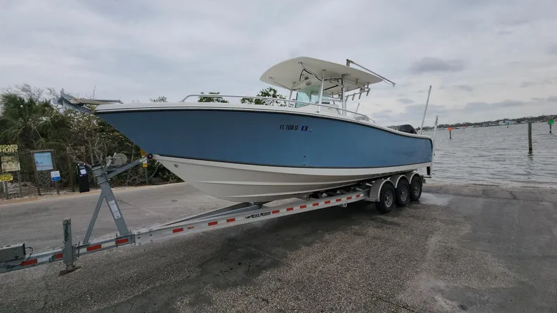 Slide: The Image of 2019 Mako 284 CC boat on trailer by waterfront, overcast sky. - 10