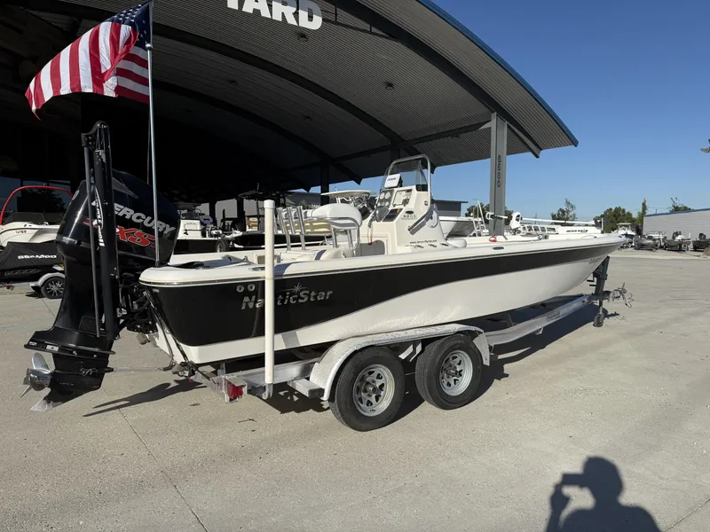 Slide: The Image of 2013 NauticStar 2200 T boat on trailer with American flag, parked outdoors. - 13
