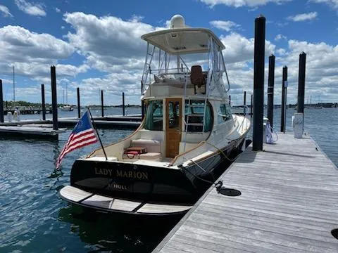 Slide: The Image of 2003 Hinckley Talaria 44 FB yacht docked, displaying an American flag, under a partly cloudy sky. - 0
