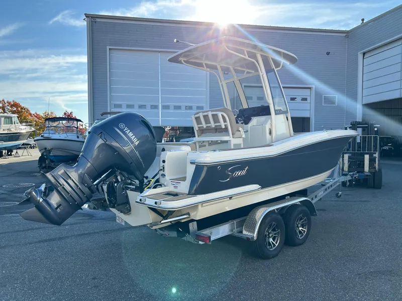 Slide: The Image of 2024 Scout 215 XSF boat with Yamaha engine on trailer, parked outside a warehouse. - 2