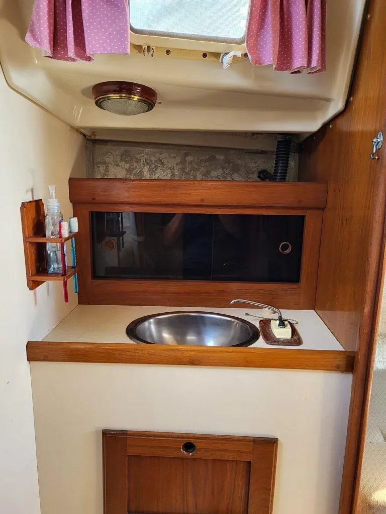 Slide: The Image of 1979 O'Day 28 sailboat interior with sink and storage, featuring pink curtains. - 31