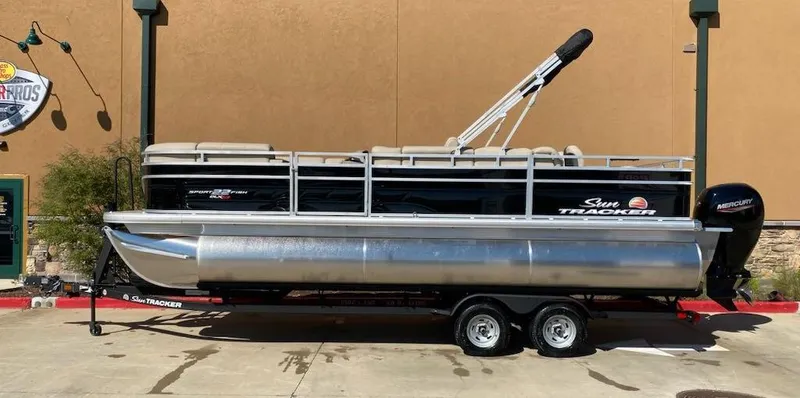 The Image of 2025 Sun Tracker SportFish 22 XP3 pontoon boat on trailer, parked outdoors. - 0