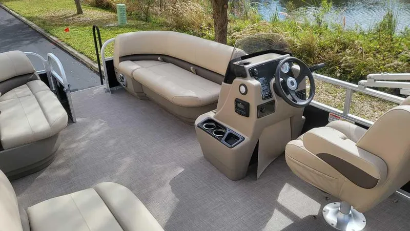 Slide: The Image of 2025 Sun Tracker Party Barge 16 DLX interior with beige seating and steering console. - 2
