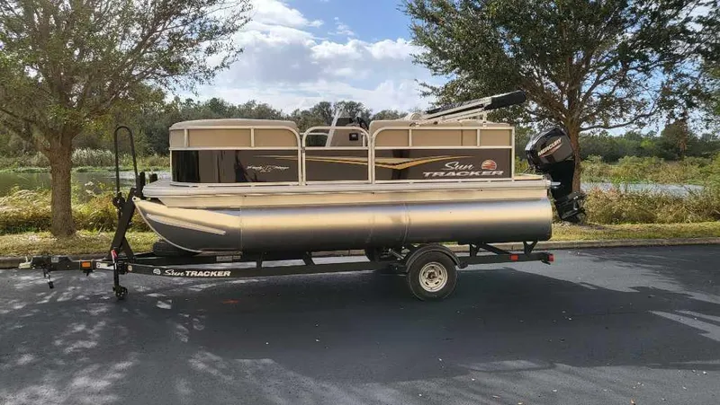 Slide: The Image of 2025 Sun Tracker Party Barge 16 DLX pontoon boat on trailer, parked outdoors. - 4