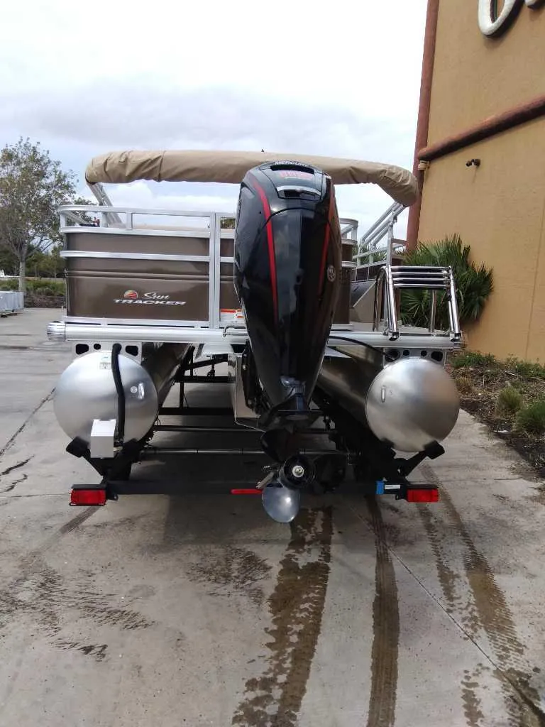 Slide: The Image of 2025 Sun Tracker SportFish 22 DLX pontoon boat, rear view with motor, parked outdoors. - 5