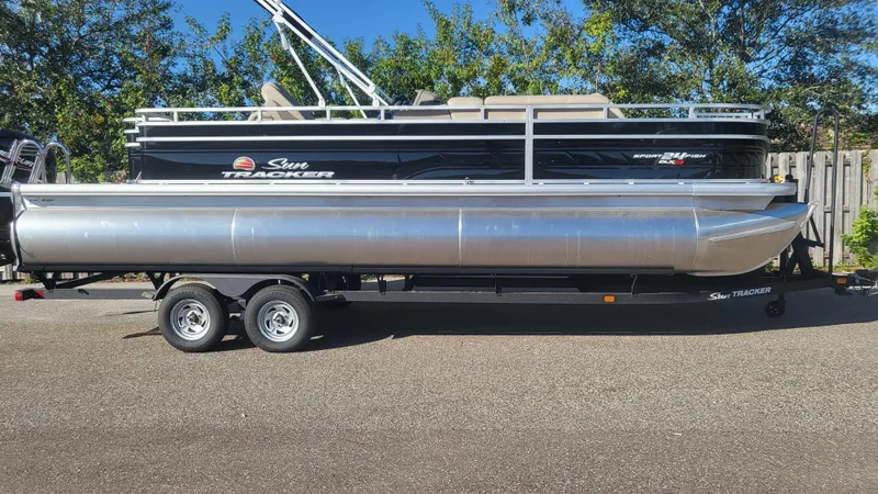 Slide: The Image of 2025 Sun Tracker Sportfish 24 XP3 pontoon boat on trailer, parked outdoors. - 2