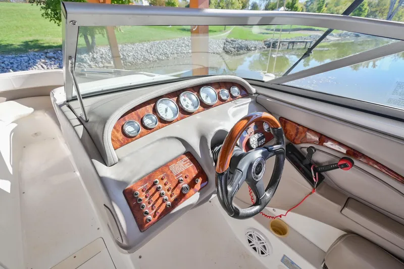 Slide: The Image of 2002 Cobalt 262 boat dashboard with wood accents and steering wheel by a lake. - 26