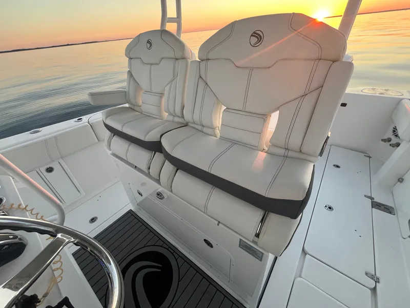 Slide: The Image of Edgewater 340CC 2022 boat interior with white seats at sunset on calm water. - 22