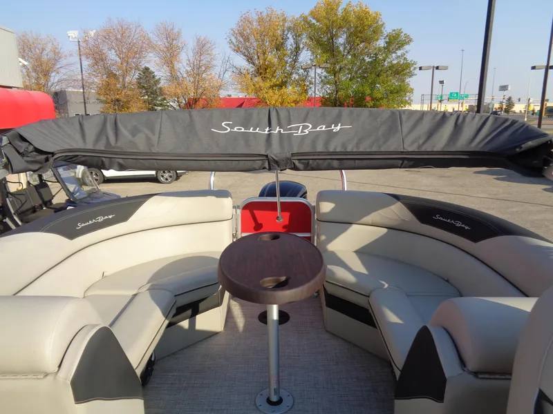 Slide: The Image of 2022 South Bay 222RS pontoon boat interior with seating and table, parked outdoors. - 12