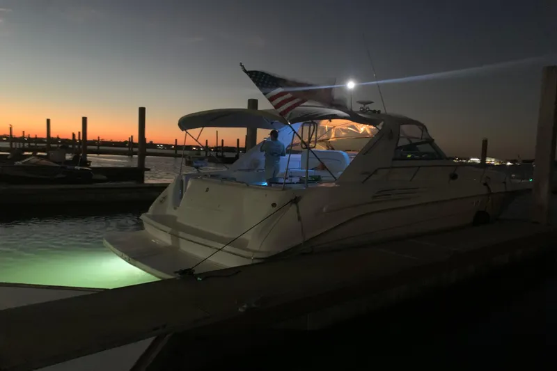 Slide: The Image of 1998 Sea Ray 450 Sundancer docked at sunset with illuminated interior and American flag. - 5