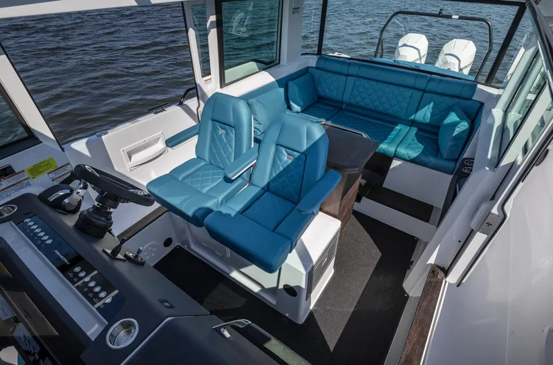 Slide: The Image of 2023 Axopar 37 XC Cross Cabin Wet Bar interior with blue seating and helm, on water. - 12