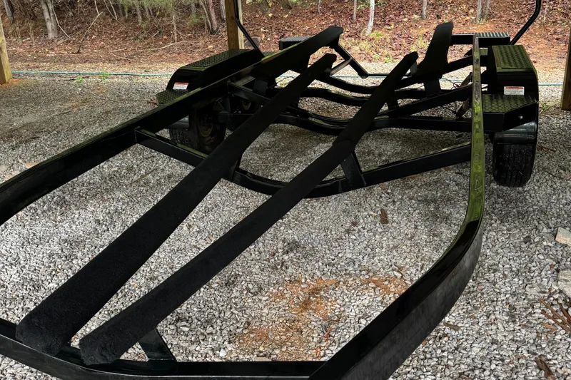 Slide: The Image of 2022 MasterCraft XT23 boat trailer on gravel, surrounded by trees. - 4