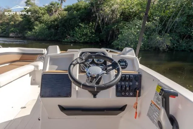 Slide: The Image of 2022 Starcraft SVX 191 OB boat dashboard with steering wheel and controls, surrounded by lush greenery. - 9