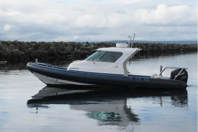 Slide: The Image of 2007 Protector Targa 28 boat on calm water, rocky shoreline in background. - 10