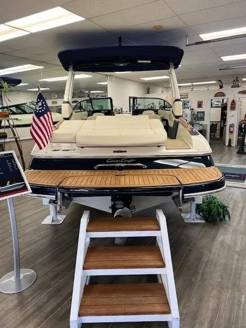 Slide: The Image of 2025 Chris-Craft Sportster 25 boat in showroom with American flag and wooden steps. - 10