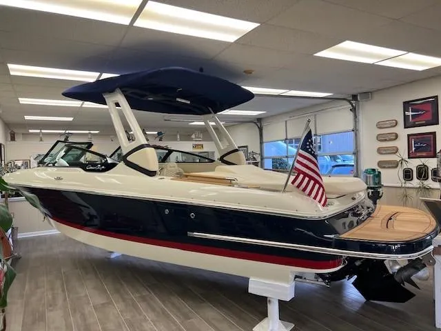 Slide: The Image of 2025 Chris-Craft Sportster 25 boat in showroom with American flag. - 2