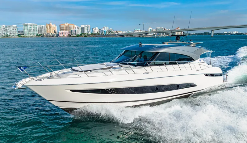 Slide: The Image of 2025 Riviera 5400 Sport Yacht cruising on open water, cityscape in background. - 10