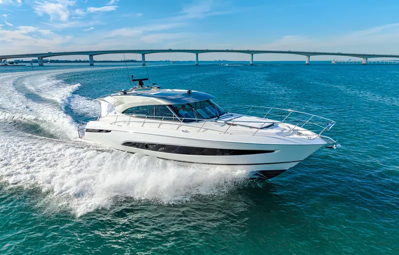 Slide: The Image of 2025 Riviera 5400 Sport Yacht cruising on blue water near a bridge. - 26