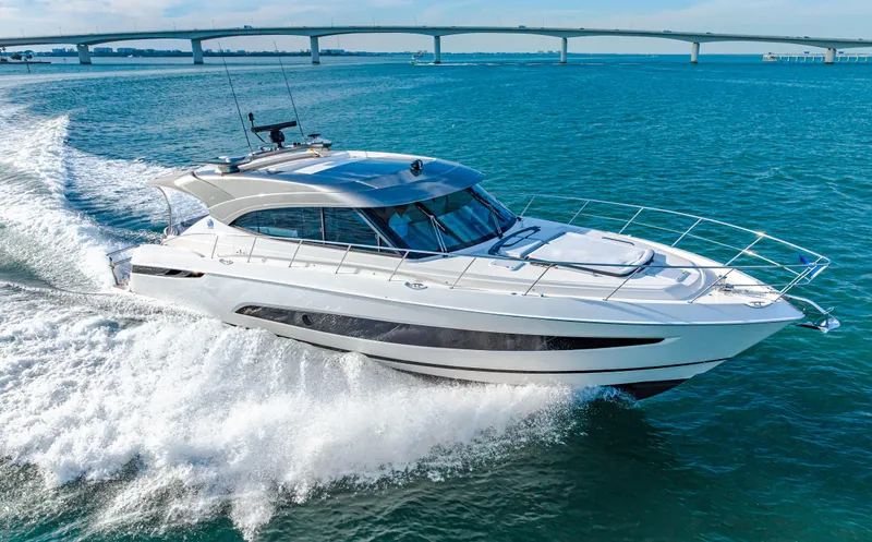 Slide: The Image of 2025 Riviera 5400 Sport Yacht cruising on open water, bridge in background. - 27