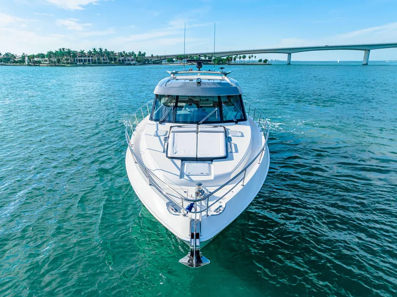 Slide: The Image of 2025 Riviera 5400 Sport Yacht cruising on clear blue water near a bridge. - 8