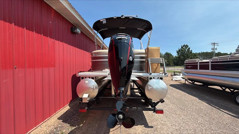 Slide: The Image of 2025 Sun Tracker Party Barge 22 DLX pontoon boat with outboard motor, parked near a red building. - 4