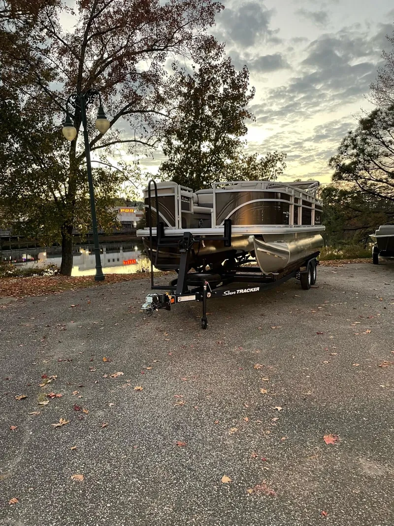 The Image of 2025 Sun Tracker SportFish 20 DLX pontoon boat parked on a scenic lakeside road. - 0