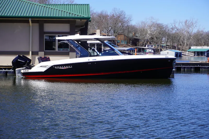 Slide: The Image of 2025 Monterey Elite 30 OB boat docked on calm water near a marina. - 0