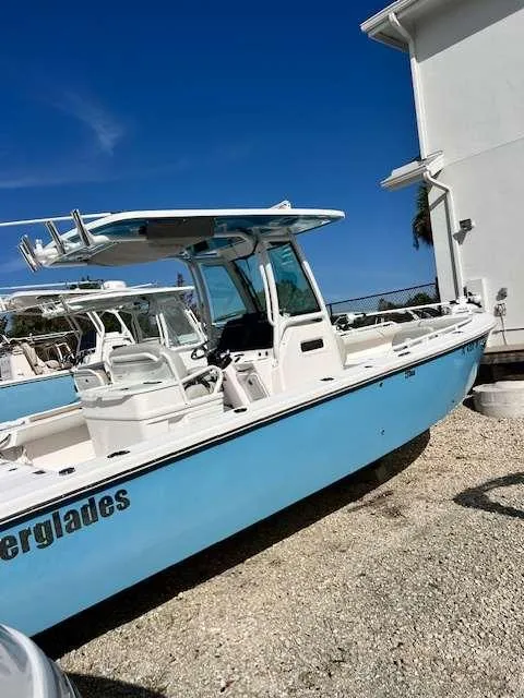 Slide: The Image of 2022 Everglades 273 CC boat in light blue, parked outdoors on gravel. - 13