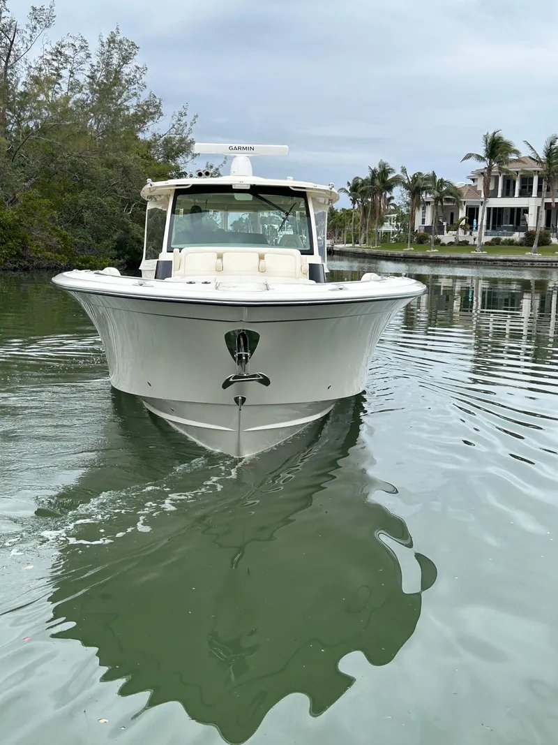 Slide: The Image of 2024 Grady-White Canyon 456 boat on calm water, surrounded by trees and luxury homes. - 2