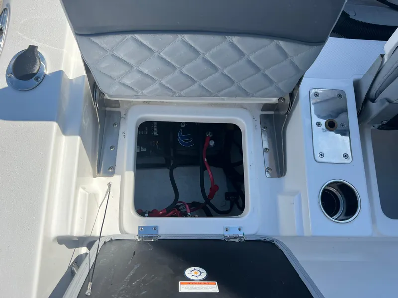 Slide: The Image of 2025 NauticStar 224 Bay boat seat storage compartment with visible wiring and cup holder. - 40