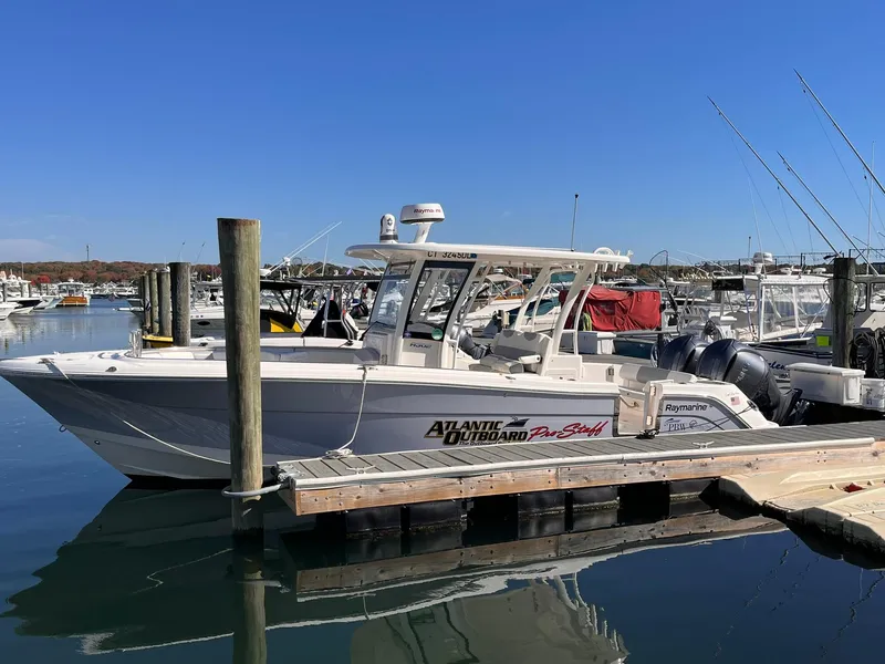 Slide: The Image of 2023 Robalo R302 Center Console boat docked in a marina under clear blue skies. - 2