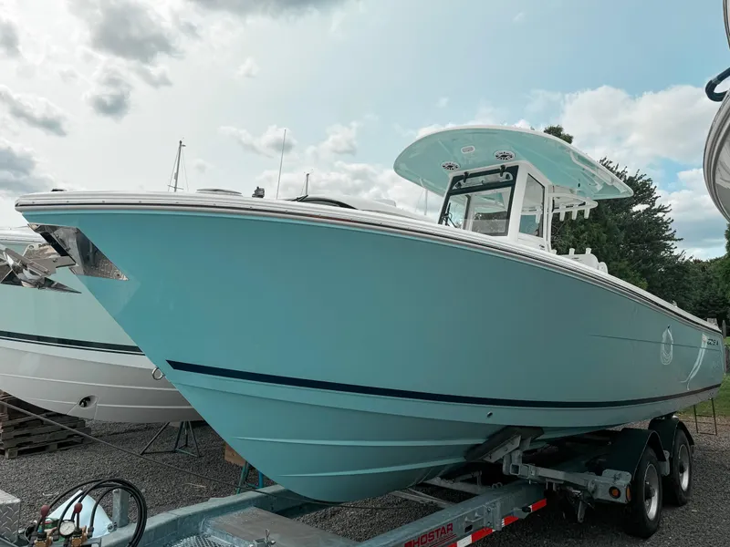 The Image of 2025 Cobia 285 Center Console boat on trailer, light blue hull, cloudy sky background. - 0