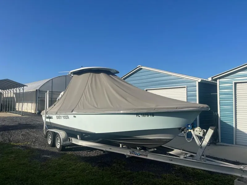 Slide: The Image of 2022 Everglades 243 Center Console boat on trailer, covered, parked near blue sheds. - 2