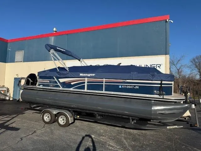Slide: The Image of 2021 Ranger RP243C pontoon boat on trailer, parked outside a building. - 0
