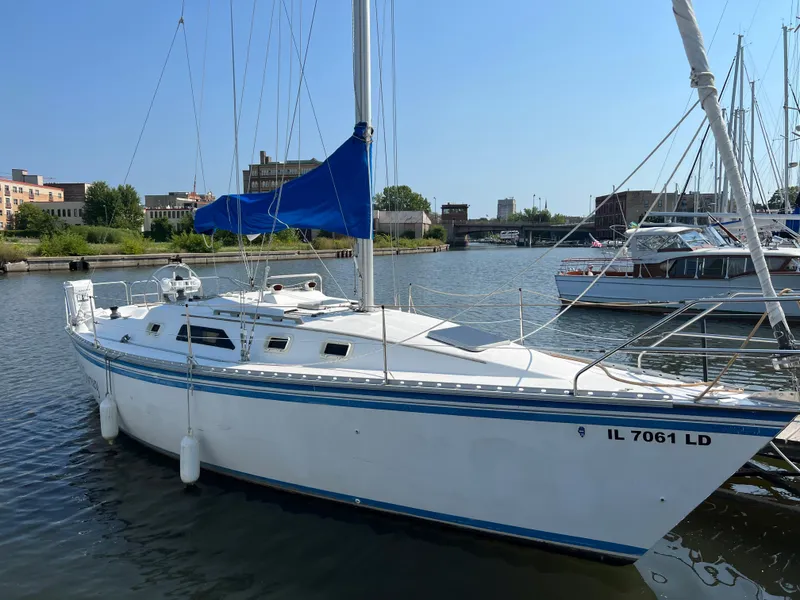 Slide: The Image of 1986 Hunter 31 sailboat docked in a marina, blue sail cover, calm water. - 1