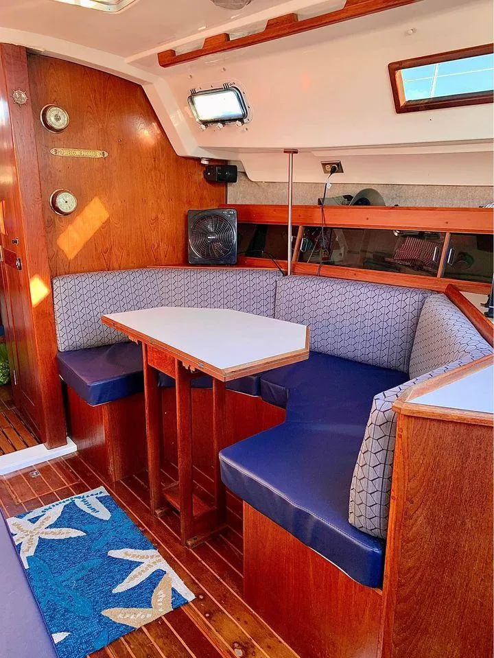 Slide: The Image of 1986 Hunter 31 sailboat interior with wooden dining area and blue cushioned seating. - 29