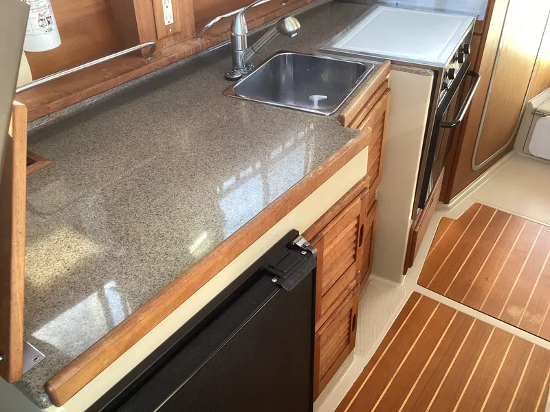 Slide: The Image of 2012 Ranger Tugs R-27 boat kitchen with sink, stove, and wooden cabinetry. - 19