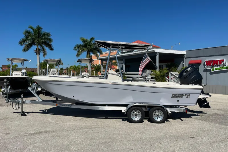 Slide: The Image of 2025 Carolina Skiff 21 Ultra Elite boat on trailer, parked outdoors with palm trees. - 7
