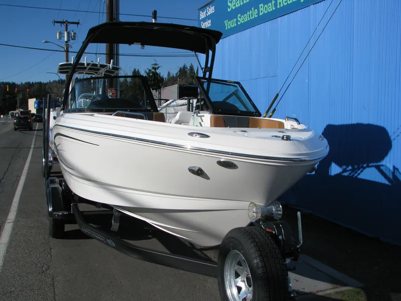 Slide: The Image of 2025 Chaparral 21 SSi boat on trailer, parked by a blue building. - 2