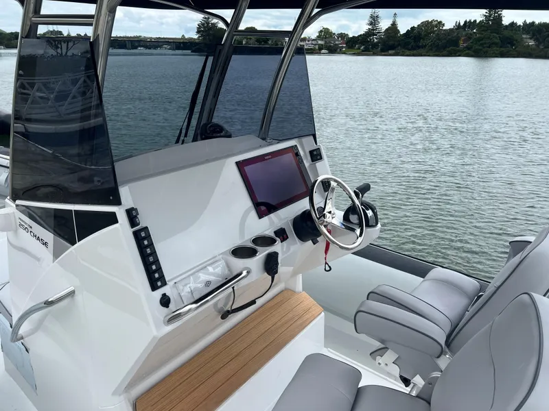 Slide: The Image of 2023 Protector 250 Chase boat interior with steering wheel and seating on a calm lake. - 2