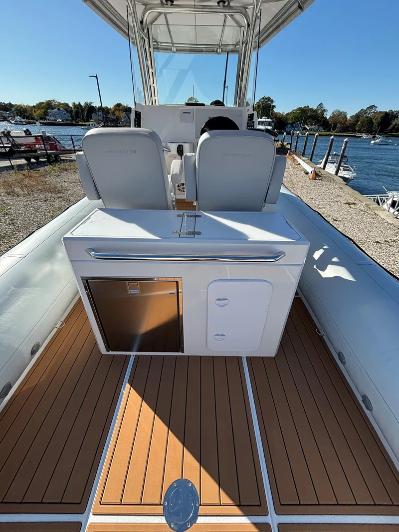 Slide: The Image of 2024 Protector 330 Chase boat interior with seating and storage, docked by a scenic waterfront. - 16